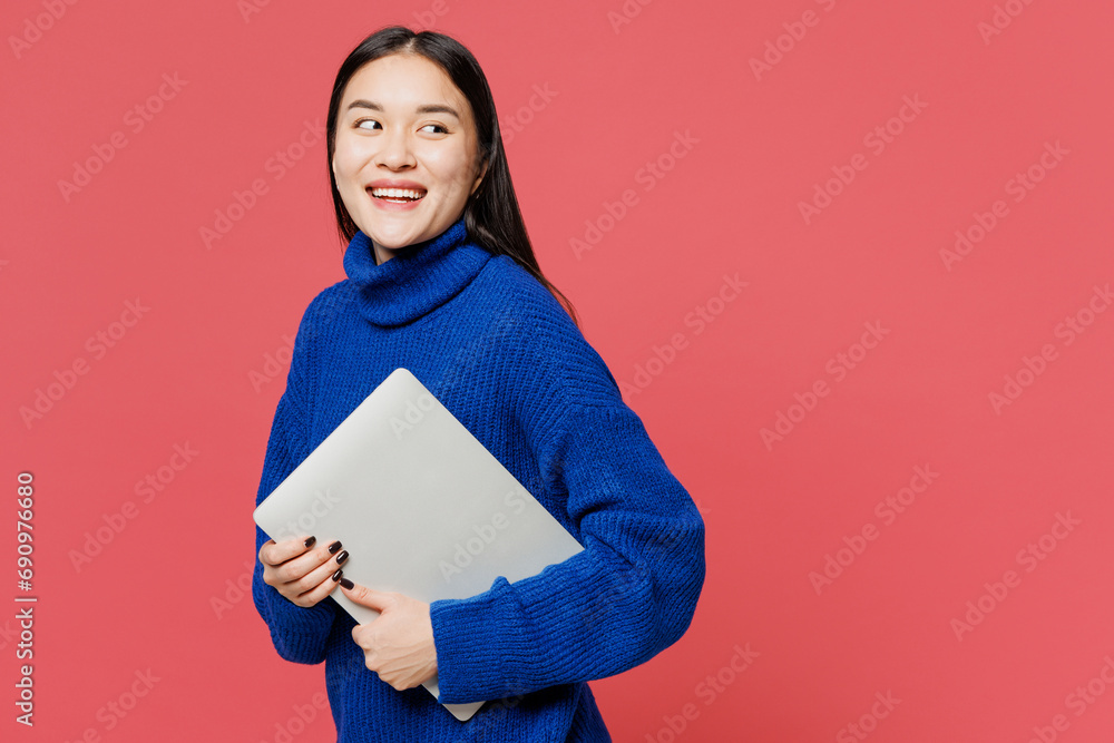 Side view young IT woman of Asian ethnicity she wearing blue sweater casual clothes holding closed laptop pc computer isolated on plain pastel light pink background studio portrait. Lifestyle concept. Side view young IT woman of Asian ethnicity she wearing blue sweater casual clothes holding closed laptop pc computer isolated on plain pastel light pink background studio portrait. Lifestyle concept.