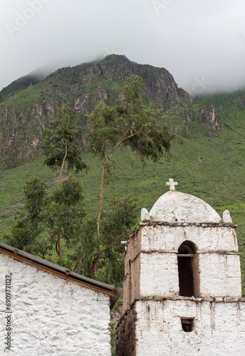 White Bell tower of a Christian church in a village around Sangalle, Canyon de Colca, Peru. Andes mountains in the background with fog. photo