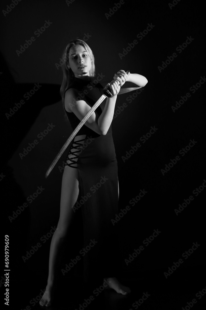 Full length low key black and white portrait of a woman with a sword