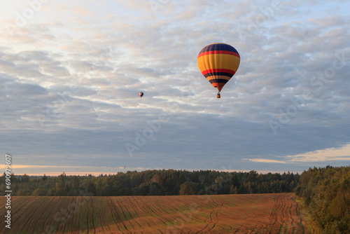 Two hot air balloons with people are flying over forests and fields in the morning at dawn © Uladzimir