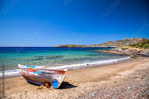 Fototapeta Naklejka Na Ścianę i Meble -  Cute dog lying on a beautiful sandy beach next to an old traditional wooden fisher boat in Syros island, Greece