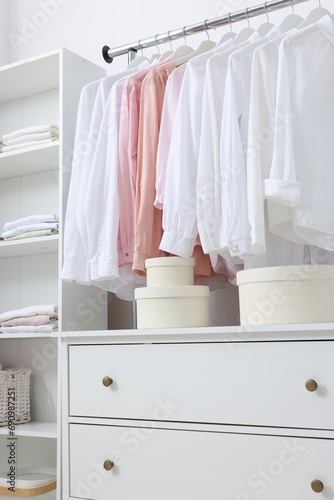 Wardrobe organization. Rack with different stylish clothes, shelving unit and chest of drawers indoors