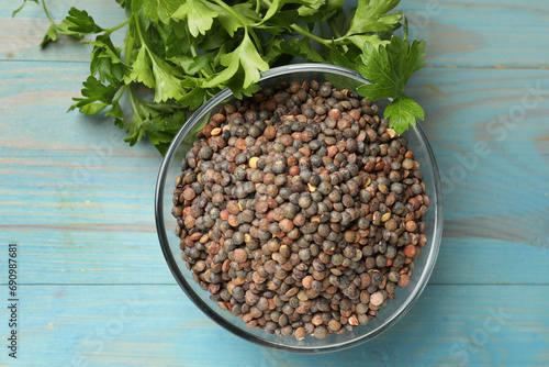 Raw lentils in bowl and parsley on light blue wooden table, top view photo