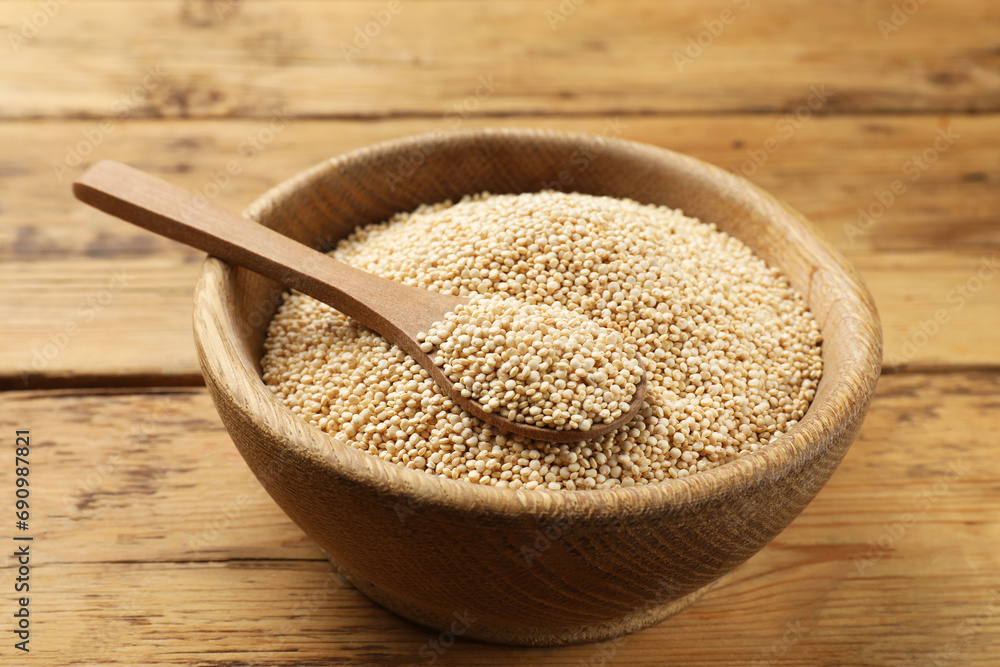 Dry quinoa seeds and spoon in bowl on wooden table, closeup Dry quinoa seeds and spoon in bowl on wooden table, closeup