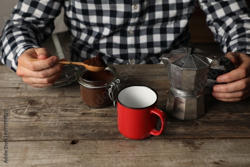 Man with moka pot and ground coffee at wooden table, closeup