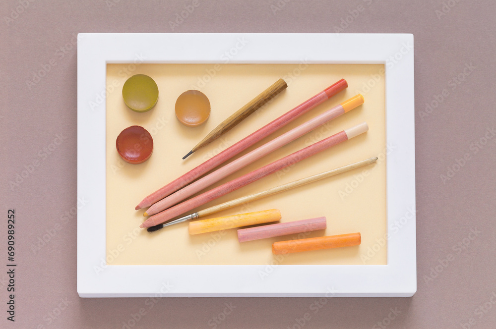 Naklejka premium Drawing and creativity as a hobby. Pencils, watercolor paints, brush and pastel sticks in warm pink and peach tones in a white frame. Shades of trendy color Peach Fuzz. Flat lay, close-up, top view