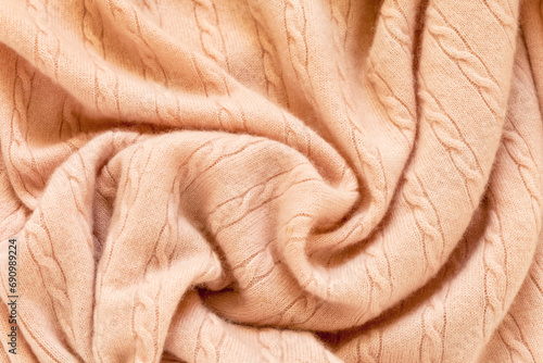 Textile background in beautiful pastel peach or trendy Peach Fuzz color. Soft, fluffy, warm mohair jumper with traditional braid pattern in soft pleats. Texture of cozy clothes from merino wool photo