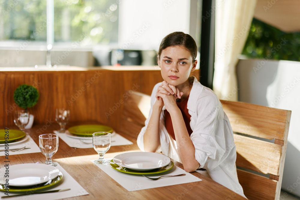 Stylish woman sitting at dining table drinking water from a glass, home modern interior, sunset light, lifestyle in comfort. Stylish woman sitting at dining table drinking water from a glass, home modern interior, sunset light, lifestyle in comfort.