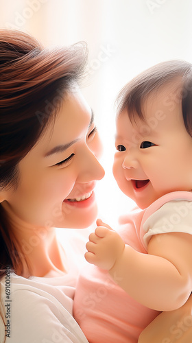 Asian mother with joyful baby, backlit by soft natural light. 