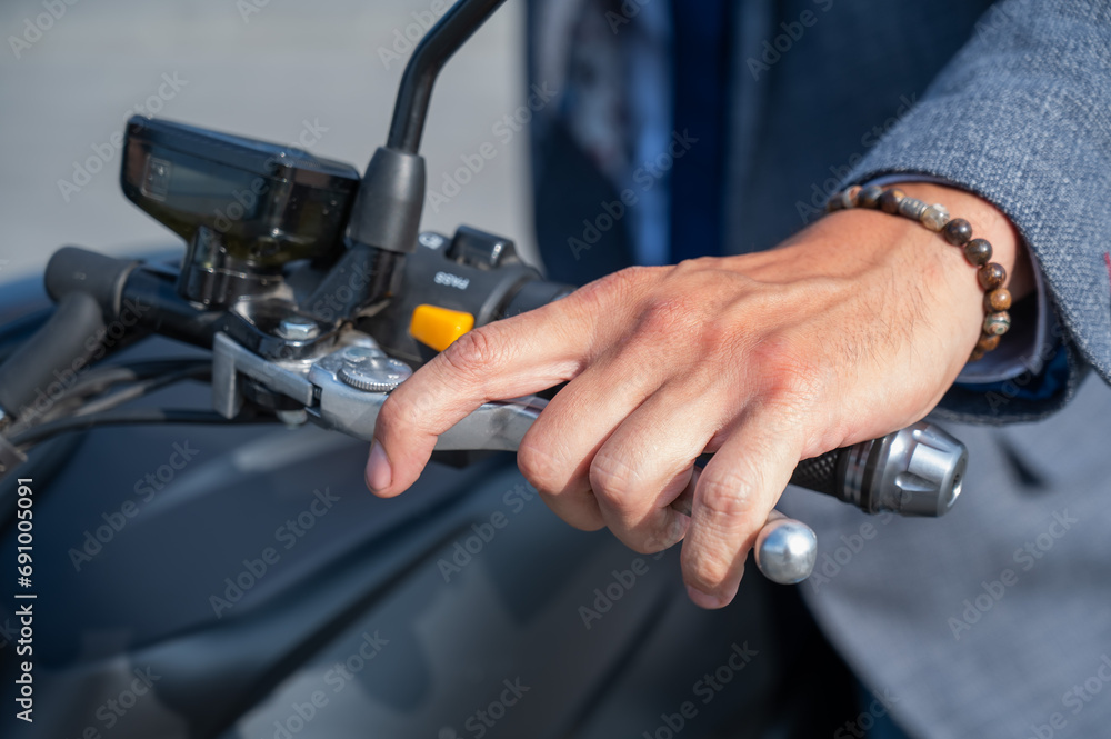 Caucasian man rides an electric motorcycle. Close-up of a man's hand pressing the brake on the steering wheel. 