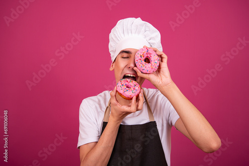 Young funny chef and pastry chef is cooking. Pink background.