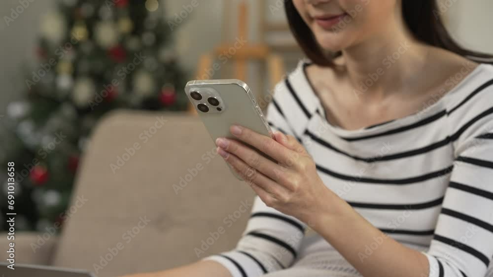 young Asian woman confidently using a smartphone, texting, chat with friends and video call sitting on a beige couch with a white cushion. young Asian woman confidently using a smartphone, texting, chat with friends and video call sitting on a beige couch with a white cushion.