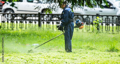 Backlit side view of a man removing grass with a trimmer