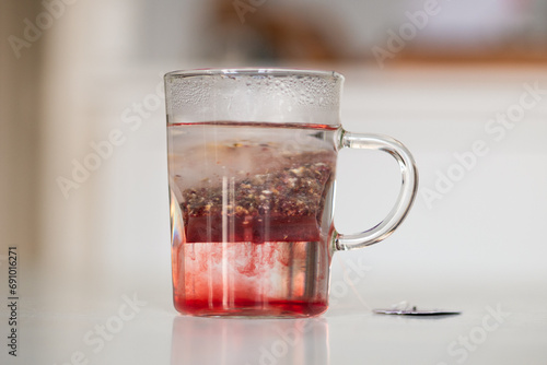 Tisane au cassis qui infuse dans une tasse transparente sur une table blanche