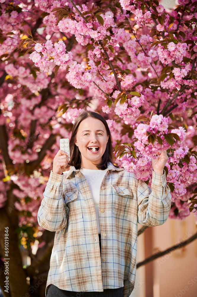 Woman allergic suffering from seasonal allergy at spring. Young happy woman applying allergy drug, posing in blossoming garden at springtime. Antihistamine medication concept Woman allergic suffering from seasonal allergy at spring. Young happy woman applying allergy drug, posing in blossoming garden at springtime. Antihistamine medication concept