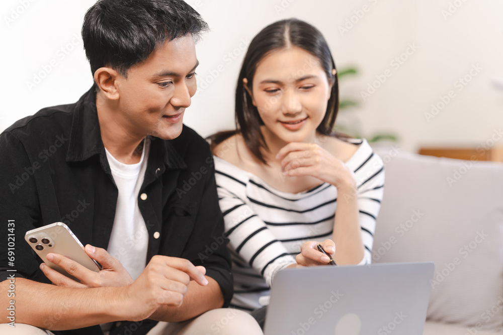 young Asian couple engaged in online shopping, wife woman holds notepad note list while husband man compares choices on smartphone. and call for price and discount, promotion. young Asian couple engaged in online shopping, wife woman holds notepad note list while husband man compares choices on smartphone. and call for price and discount, promotion.