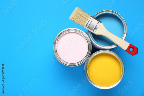 Cans of colorful paints and brush on light blue background, flat lay. Space for text
