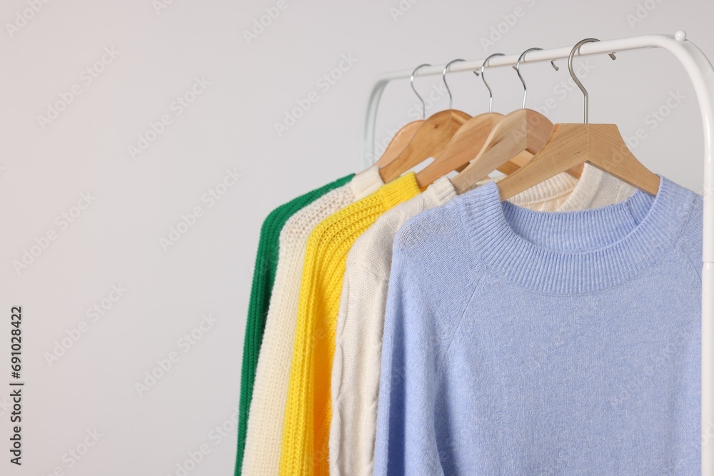 Rack with different warm sweaters on light background. Space for text Rack with different warm sweaters on light background. Space for text