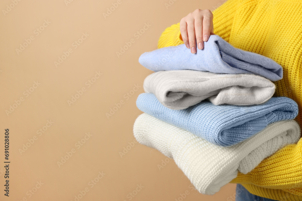 Woman with stack of casual sweaters on light brown background, closeup. Space for text Woman with stack of casual sweaters on light brown background, closeup. Space for text