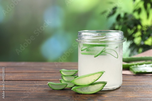 Fresh aloe juice in jar and cut leaves on wooden table outdoors, space for text