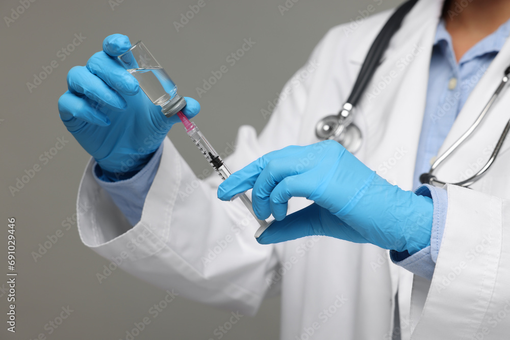 Doctor filling syringe with medication from glass vial on grey background, closeup Doctor filling syringe with medication from glass vial on grey background, closeup