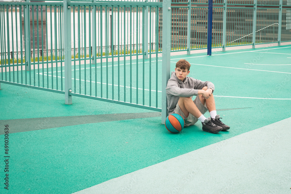 Teenage boy basketball player sitting alone at sportground