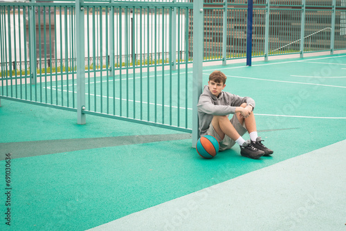 Teenage boy basketball player sitting alone at sportground photo