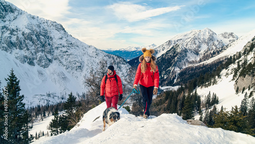 Active couple hiking on extreme terrain in the snowy mountains with their dog in winter