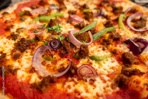Close up of a pizza in a restaurant with cheese, tomato, onion, pepper and beef