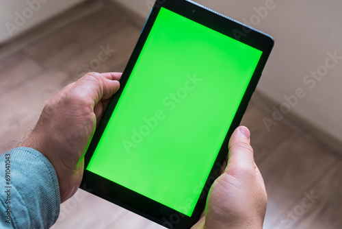 Man is holding tablet pc on his hands. Green screen mockup on the tablet. Cross view.