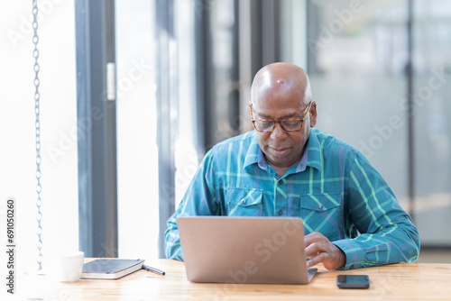 Portrait of happy African American small business owner. Millennial black smiling, sitting and using the laptop, and holding a cup of coffee work in modern office.