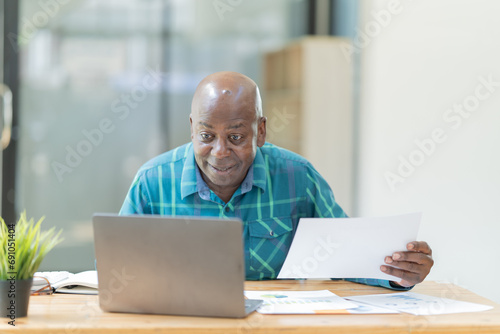 Portrait of happy African American small business owner. Millennial black smiling, sitting and using the laptop, and holding a cup of coffee work in modern office.