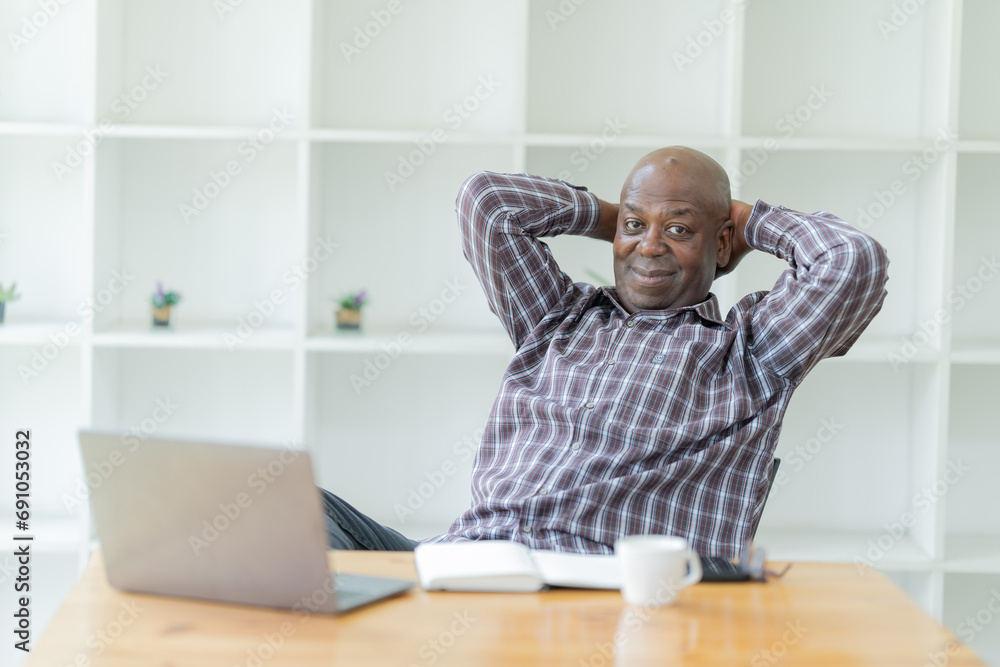 Fototapeta premium Portrait of happy African American small business owner. Millennial black smiling, sitting and using the laptop, and holding a cup of coffee work in modern office.