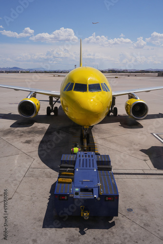 Yellow airplane and other vehicles against a vibrant sky at the airport
