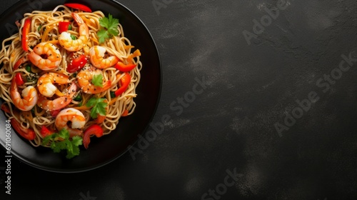 Spicy stir fried instant noodle with shrimps and thai basil leaves in black plate on dark marble . Top view