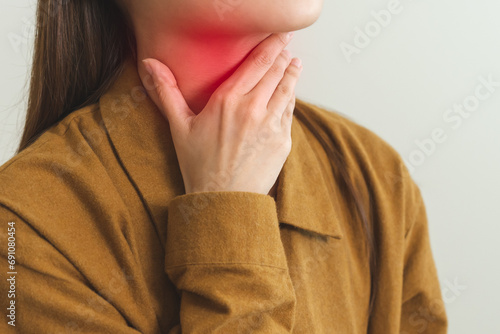 Sickness in inflaming asian young woman, girl use hand check self touch at sore throat, pain thyroid gland on neck or disease reflux, acid of suffer people on wall background. Medical and healthcare.