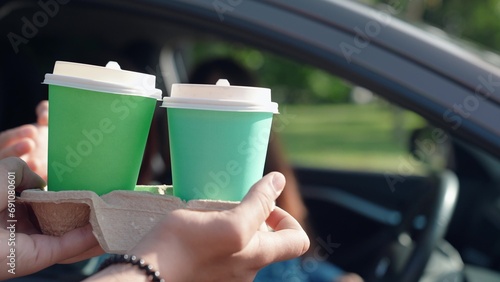 Woman driving, delivery of drinks to car. Fast food concept, hot tea delivery through car window. Delicious coffee for travelers by car. Food for driver, passenger to eat on road. Buying coffee in car