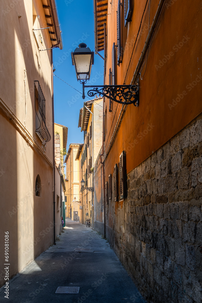 Dark narrow empty old medieval street with colorful buildings in spots of sunlight, Florence, Italy