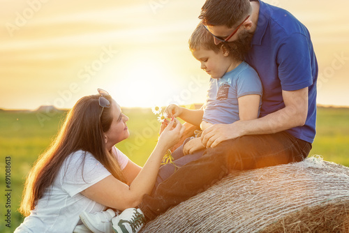 Portrait of a beautiful young family against the background of a summer sunset. Father and son pick field daisies for mother. Mom is happy with the flowers. photo