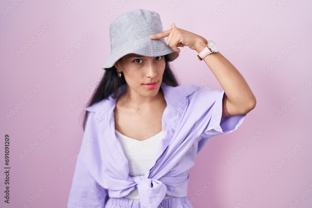 Young hispanic woman standing over pink background wearing hat pointing unhappy to pimple on forehead, ugly infection of blackhead. acne and skin problem Young hispanic woman standing over pink background wearing hat pointing unhappy to pimple on forehead, ugly infection of blackhead. acne and skin problem