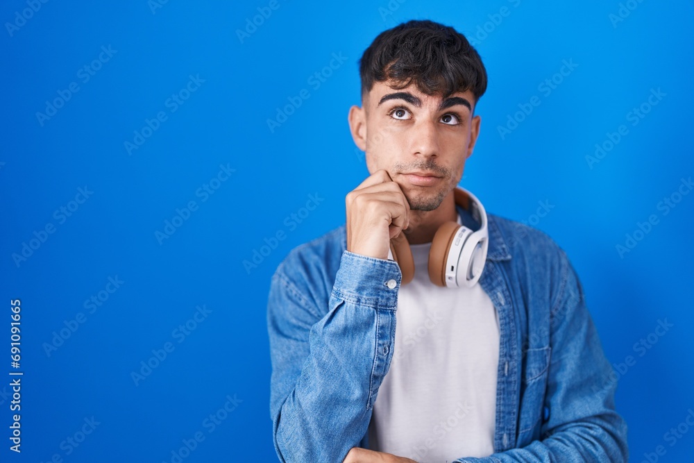Young hispanic man standing over blue background with hand on chin thinking about question, pensive expression. smiling with thoughtful face. doubt concept. Young hispanic man standing over blue background with hand on chin thinking about question, pensive expression. smiling with thoughtful face. doubt concept.