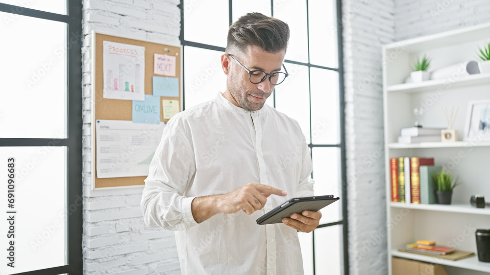 Portrait of a serious-faced young hispanic man, an attractive, successful business worker using touchpad while concentrating on his work at the office indoors. Portrait of a serious-faced young hispanic man, an attractive, successful business worker using touchpad while concentrating on his work at the office indoors.