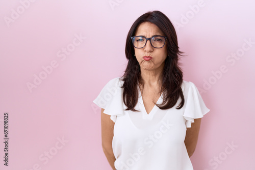 Middle age hispanic woman wearing casual white t shirt and glasses puffing cheeks with funny face. mouth inflated with air, crazy expression. photo