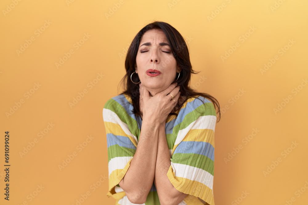 Middle age hispanic woman standing over yellow background shouting and suffocate because painful strangle. health problem. asphyxiate and suicide concept. Middle age hispanic woman standing over yellow background shouting and suffocate because painful strangle. health problem. asphyxiate and suicide concept.
