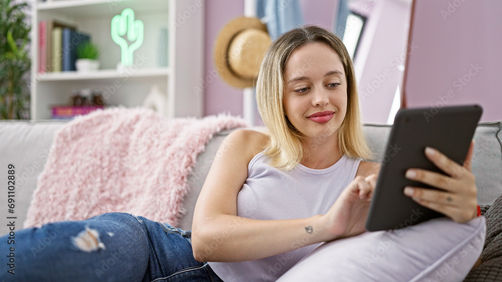 Young blonde woman using touchpad sitting on sofa at home Young blonde woman using touchpad sitting on sofa at home
