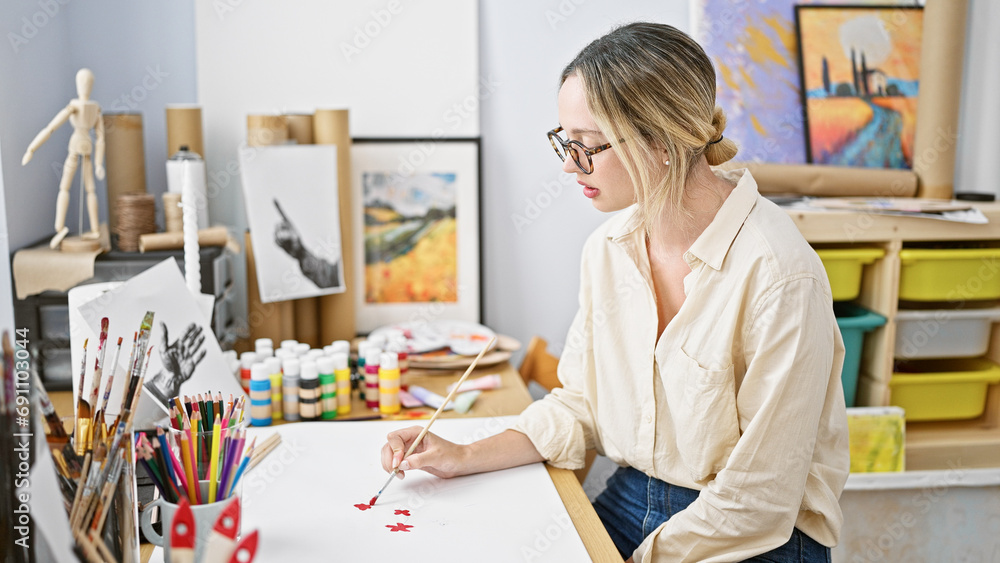 Young blonde woman artist drawing on paper sitting on table at art studio Young blonde woman artist drawing on paper sitting on table at art studio