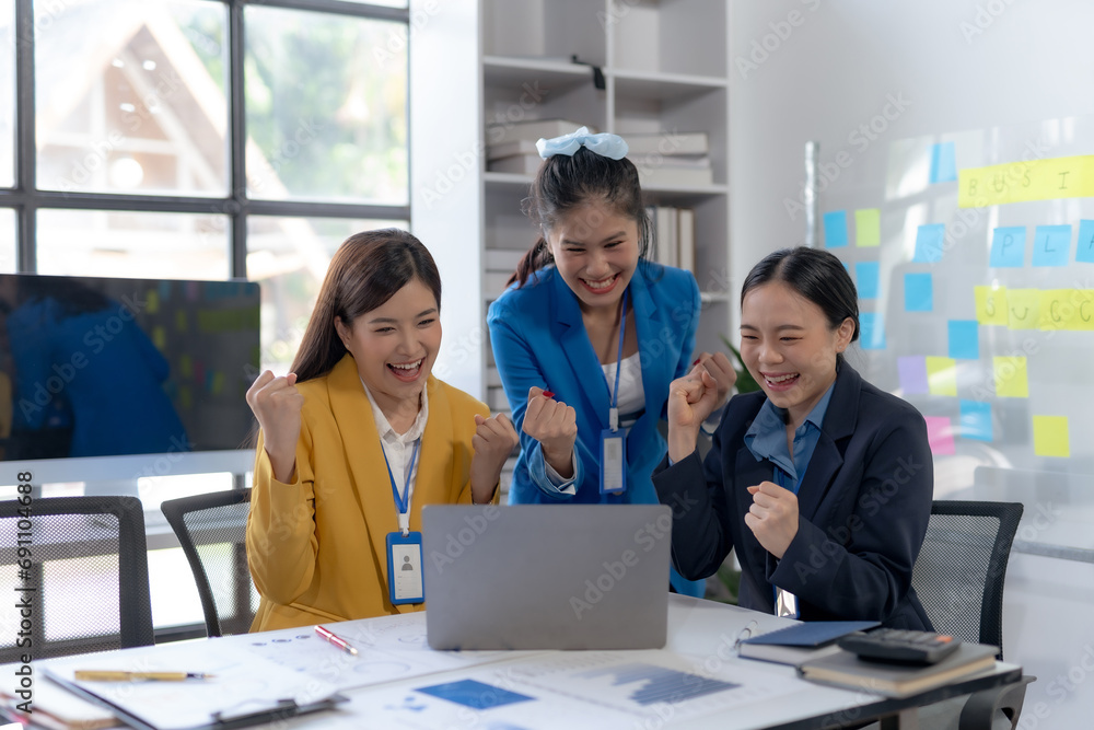 Team of young Asian business woman using laptop computer in the office, getting good news, feeling joy, laughing, making winner gesture, happy to win prize. Team of young Asian business woman using laptop computer in the office, getting good news, feeling joy, laughing, making winner gesture, happy to win prize.