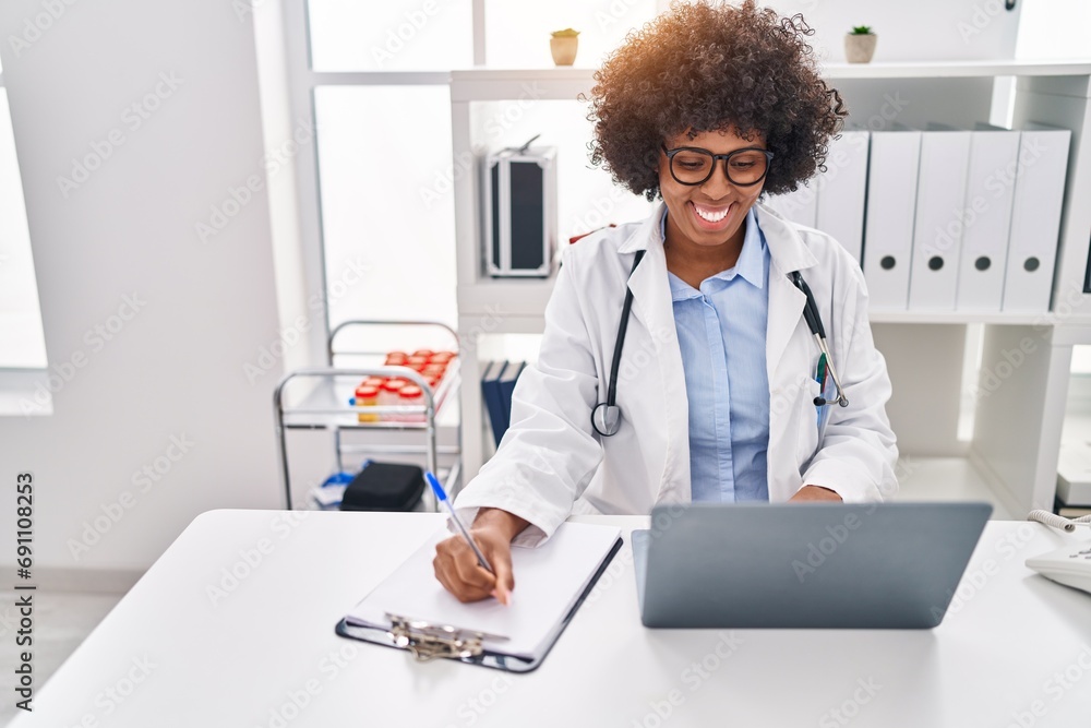African american woman doctor using laptop writing on clipboard at clinic African american woman doctor using laptop writing on clipboard at clinic