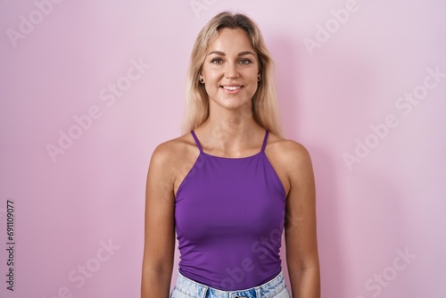 Young blonde woman standing over pink background with a happy and cool smile on face. lucky person.