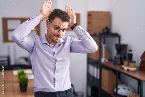Young hispanic man at the office doing bunny ears gesture with hands palms looking cynical and skeptical. easter rabbit concept. photo